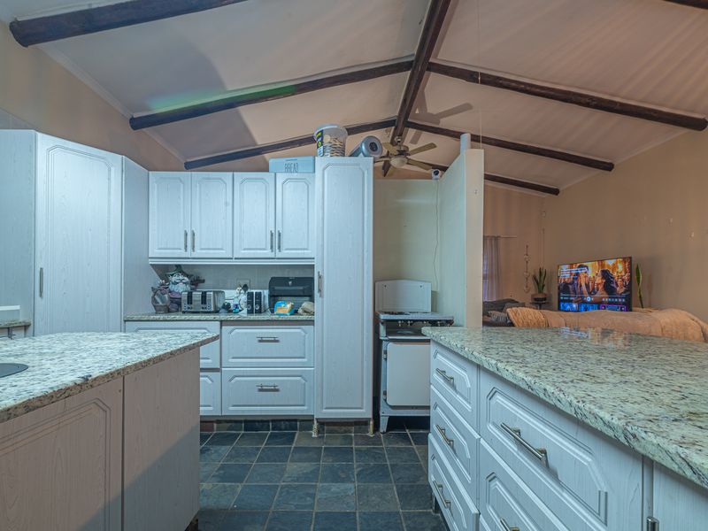 Open-plan kitchen featuring granite countertops, slate flooring, and exposed timber ceiling beams, seamlessly connecting to the adjacent living area.