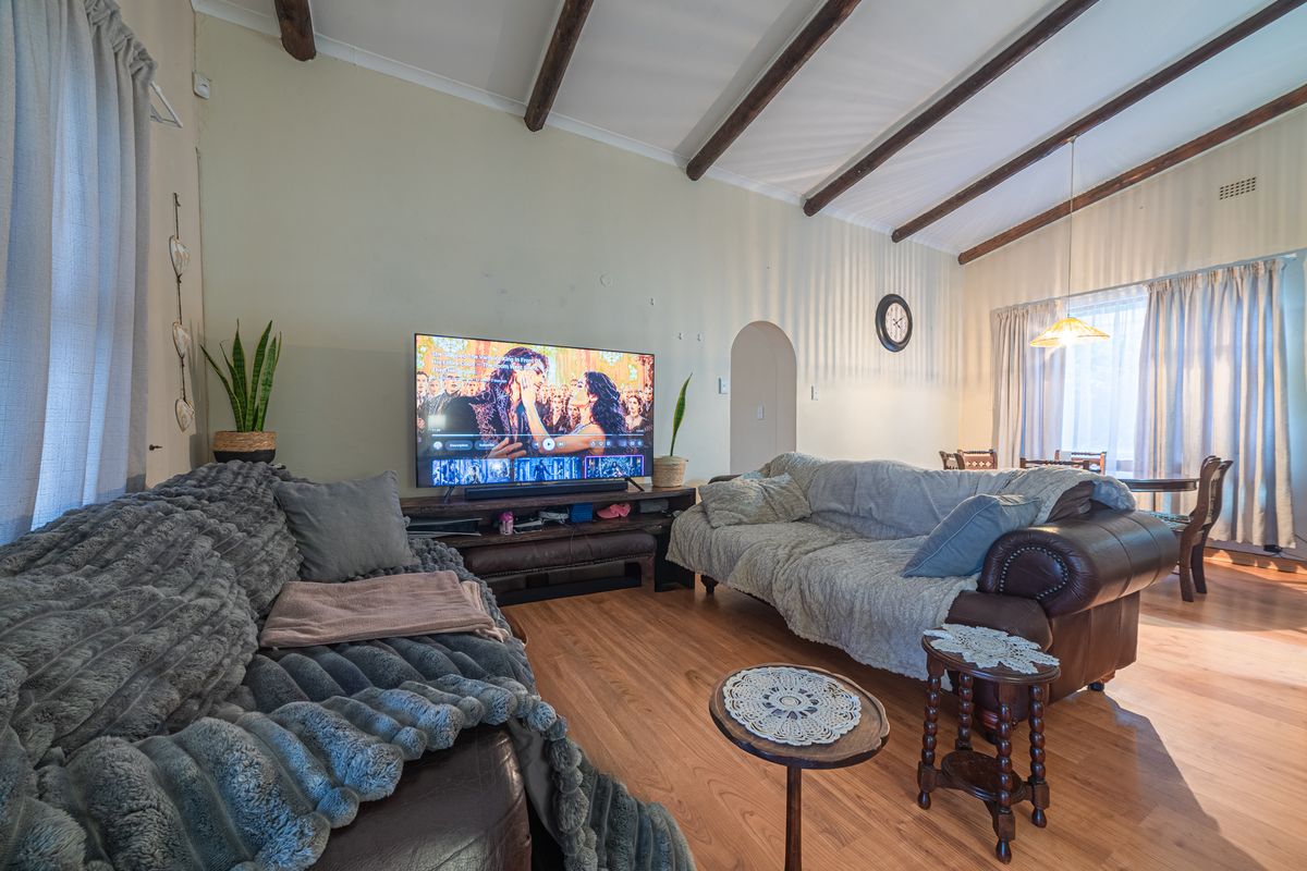 A living room featuring exposed timber ceiling beams, laminate flooring, and an arched doorway leading to adjacent living spaces.