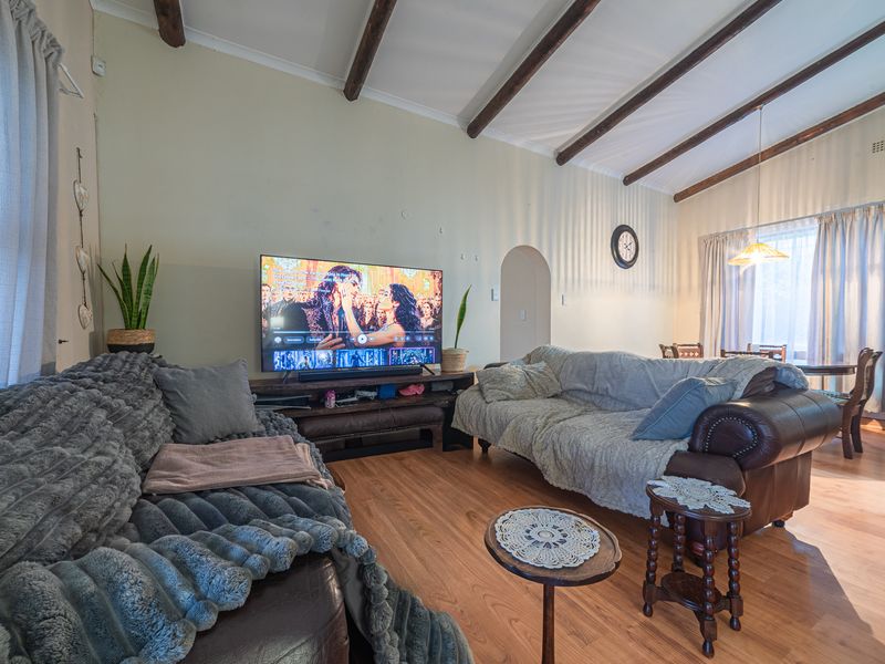 A living room featuring exposed timber ceiling beams, laminate flooring, and an arched doorway leading to adjacent living spaces.