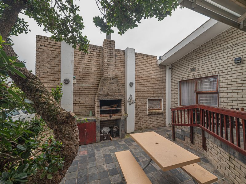 Outdoor patio area featuring a built-in brick braai, slate tile flooring, and a timber railing, providing a functional space for outdoor entertaining.