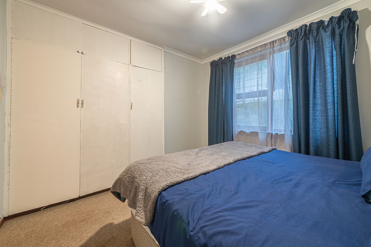 A functional bedroom featuring built-in cupboards, carpeted flooring, and a ceiling fan, offering a neutral base for potential updates.