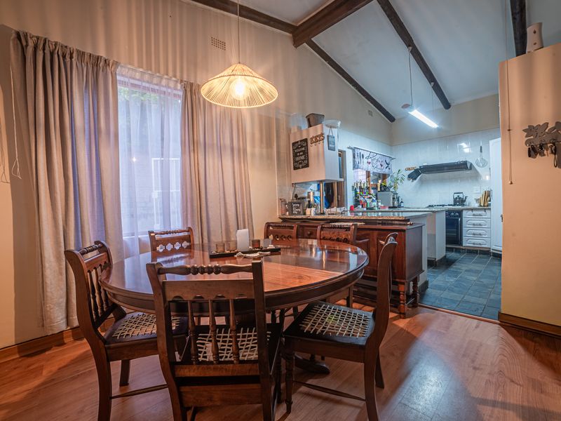 Open plan dining area featuring exposed timber beams and laminate flooring, flowing into a functional kitchen with stone countertops and tiled flooring.