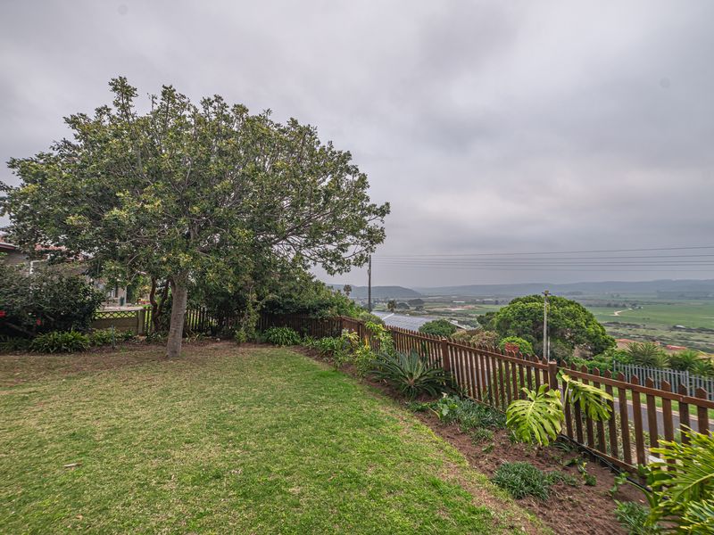 A well-maintained garden area featuring a wooden picket fence, mature trees, and established garden beds with scenic rural views in the background.