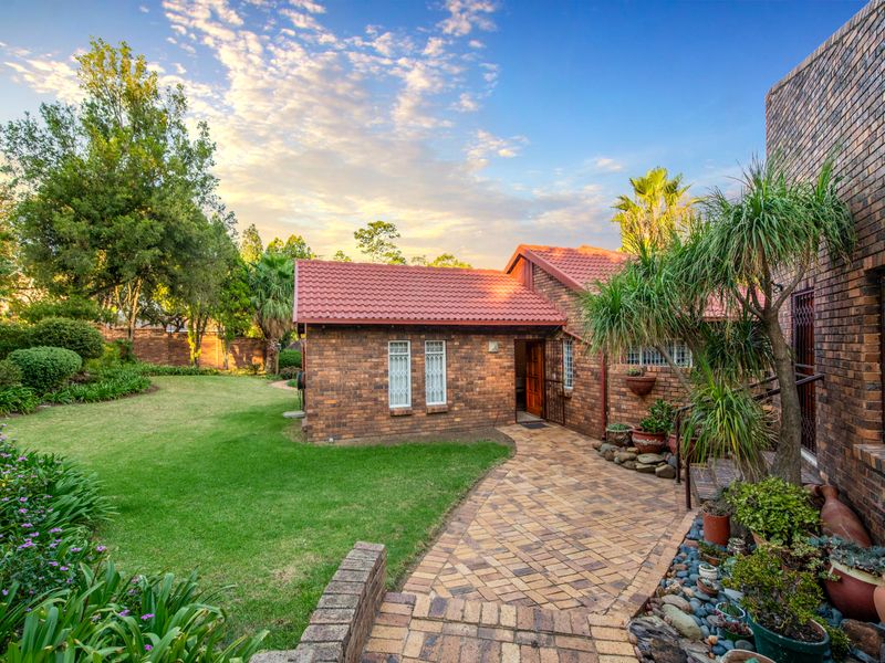 A well-maintained rear exterior view featuring a face brick facade, tiled roof, paved walkway, and a lush, landscaped garden.