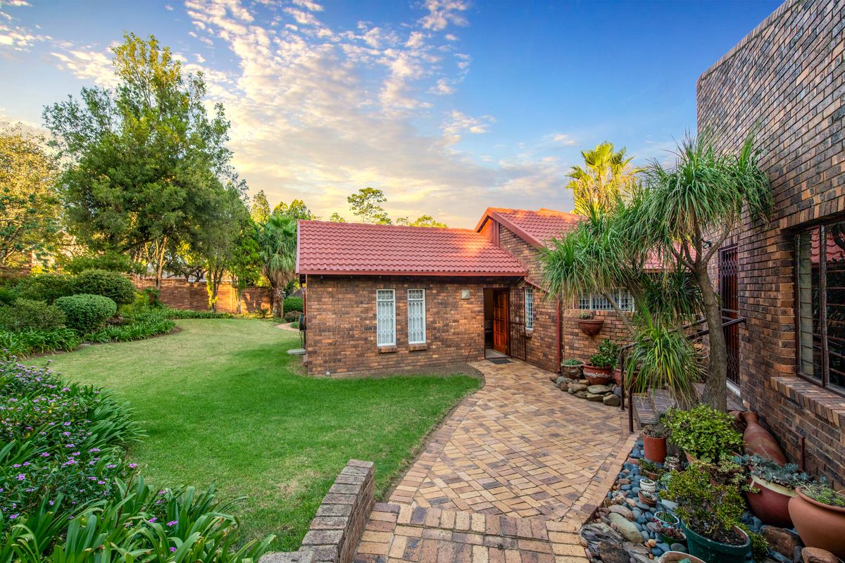 A well-maintained rear exterior view featuring a face brick facade, tiled roof, paved walkway, and a lush, landscaped garden.