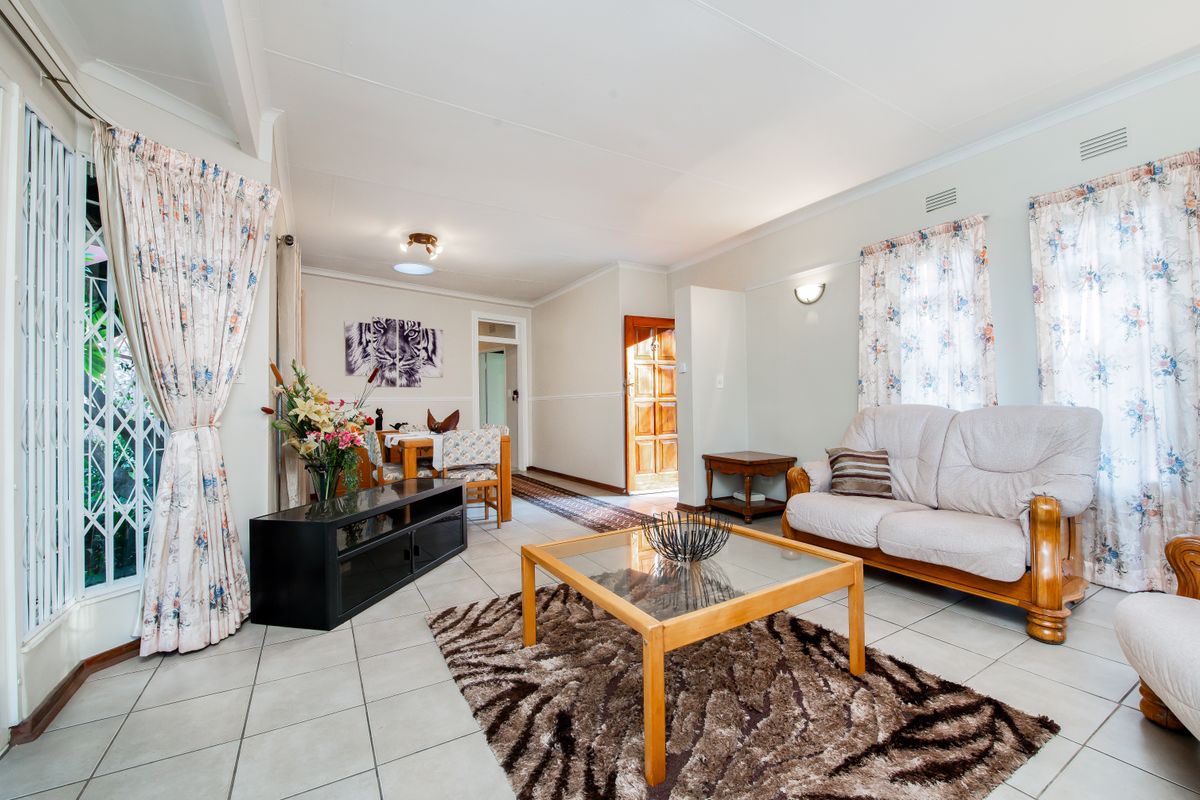 A spacious living area featuring tiled flooring, coved ceilings, and natural light through large windows with security gates.
