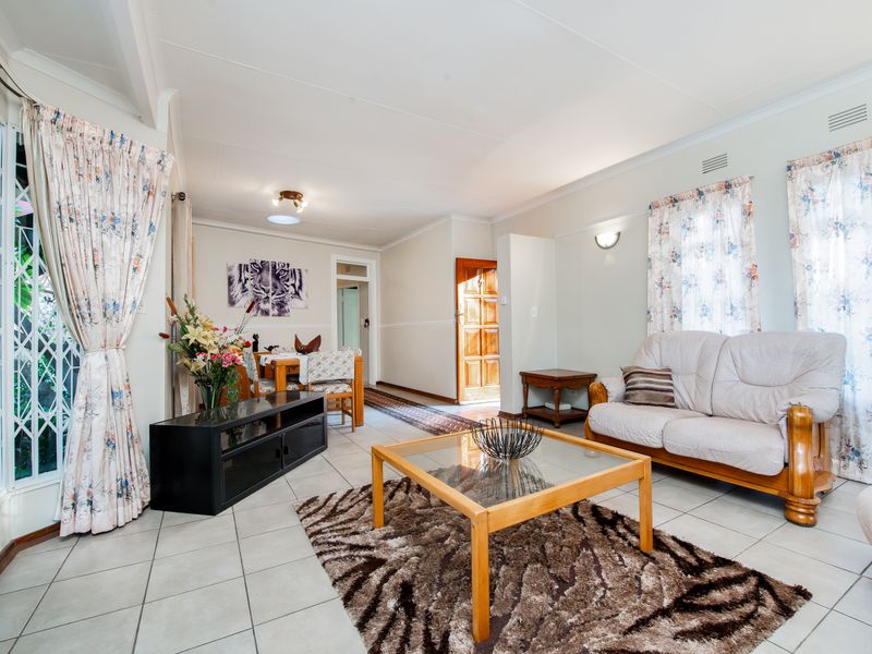 A spacious living area featuring tiled flooring, coved ceilings, and natural light through large windows with security gates.