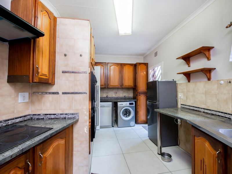 Functional kitchen featuring wooden cabinetry, granite countertops, tiled backsplash, and integrated appliances, offering a practical layout with ample storage space.