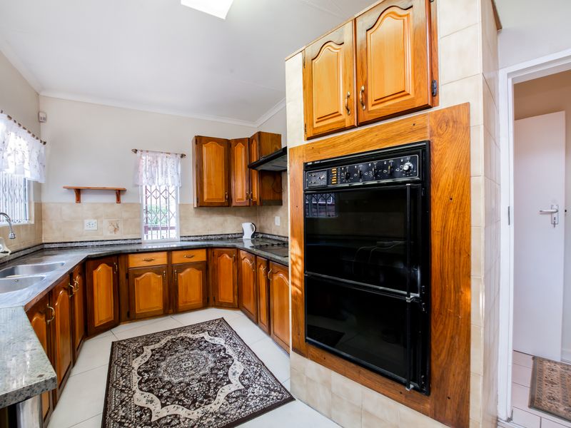A functional kitchen featuring traditional wooden cabinetry, granite countertops, a built-in double oven, and a double stainless steel sink with tiled backsplash.