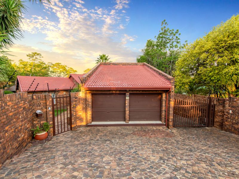 A well-maintained front exterior featuring a double garage with roller doors, a paved circular driveway, and secure brick boundary walls with electric fencing.