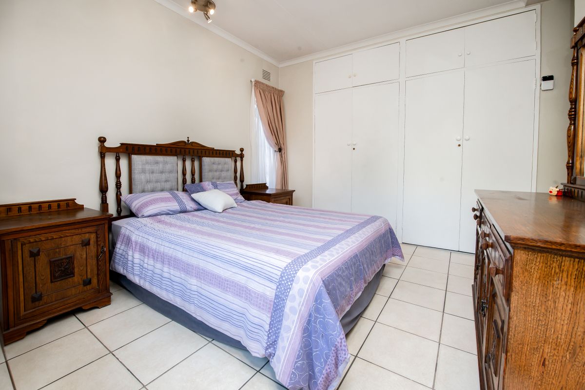 A bedroom featuring tiled flooring, built-in cupboards, and a ceiling light fixture, offering a functional space with neutral wall finishes.