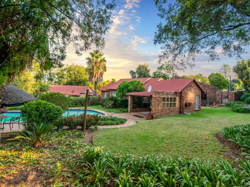 Spacious rear garden featuring a swimming pool, a thatched lapa, and a covered patio area attached to the brick-built residence.