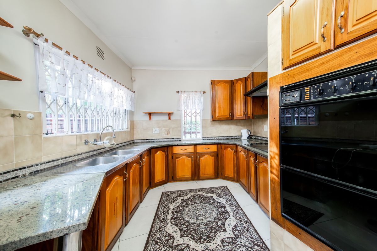 A functional kitchen featuring traditional wooden cabinetry, granite countertops, a double sink, and a built-in eye-level oven with an integrated hob and extractor.