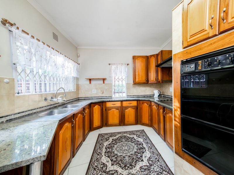 A functional kitchen featuring traditional wooden cabinetry, granite countertops, a double sink, and a built-in eye-level oven with an integrated hob and extractor.