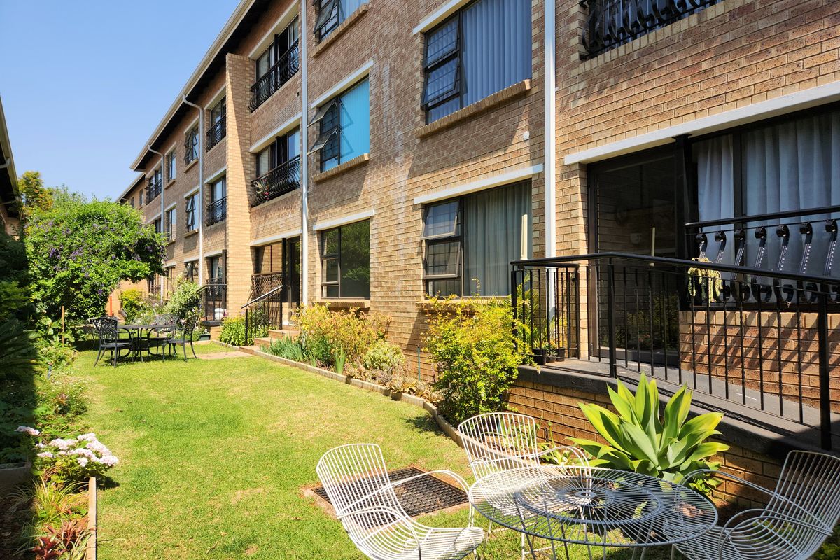 Rear view of a multi-story apartment building featuring face brick exterior, metal security railings, and ground-level access to a shared garden area.