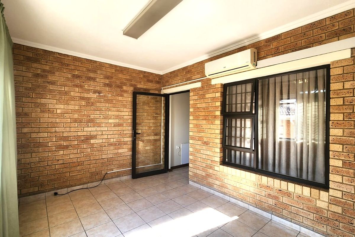 An empty living area featuring exposed brick walls, tiled flooring, and a wall-mounted air conditioning unit.