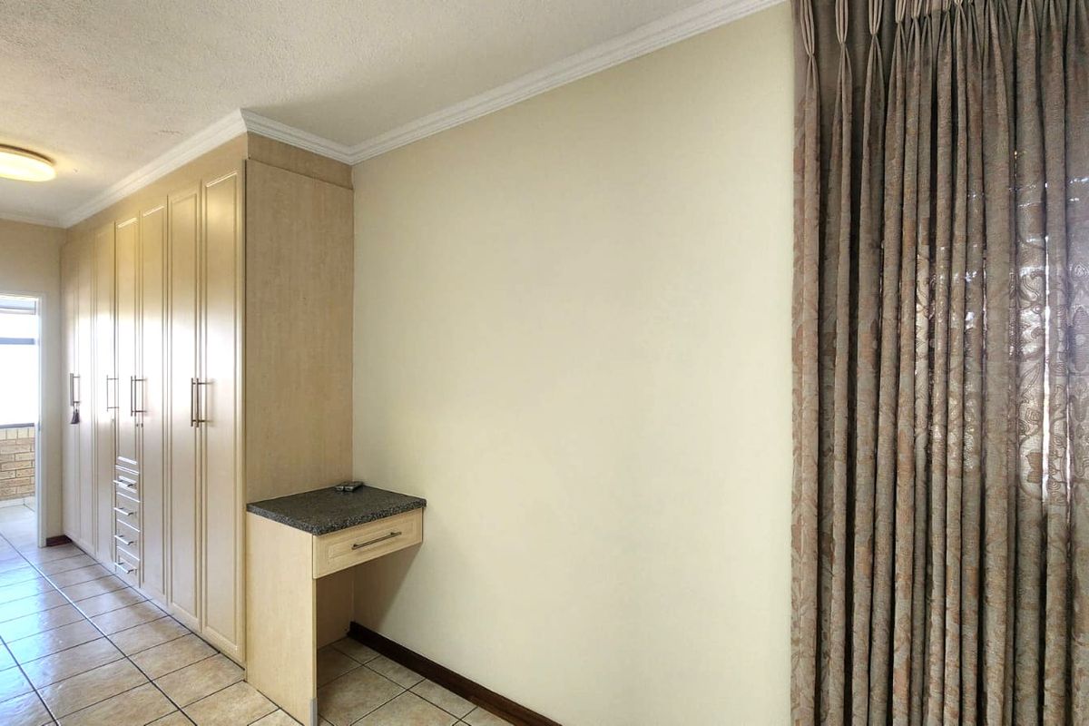 A bedroom featuring built-in cupboards with an integrated vanity unit, tiled flooring, and neutral wall finishes.