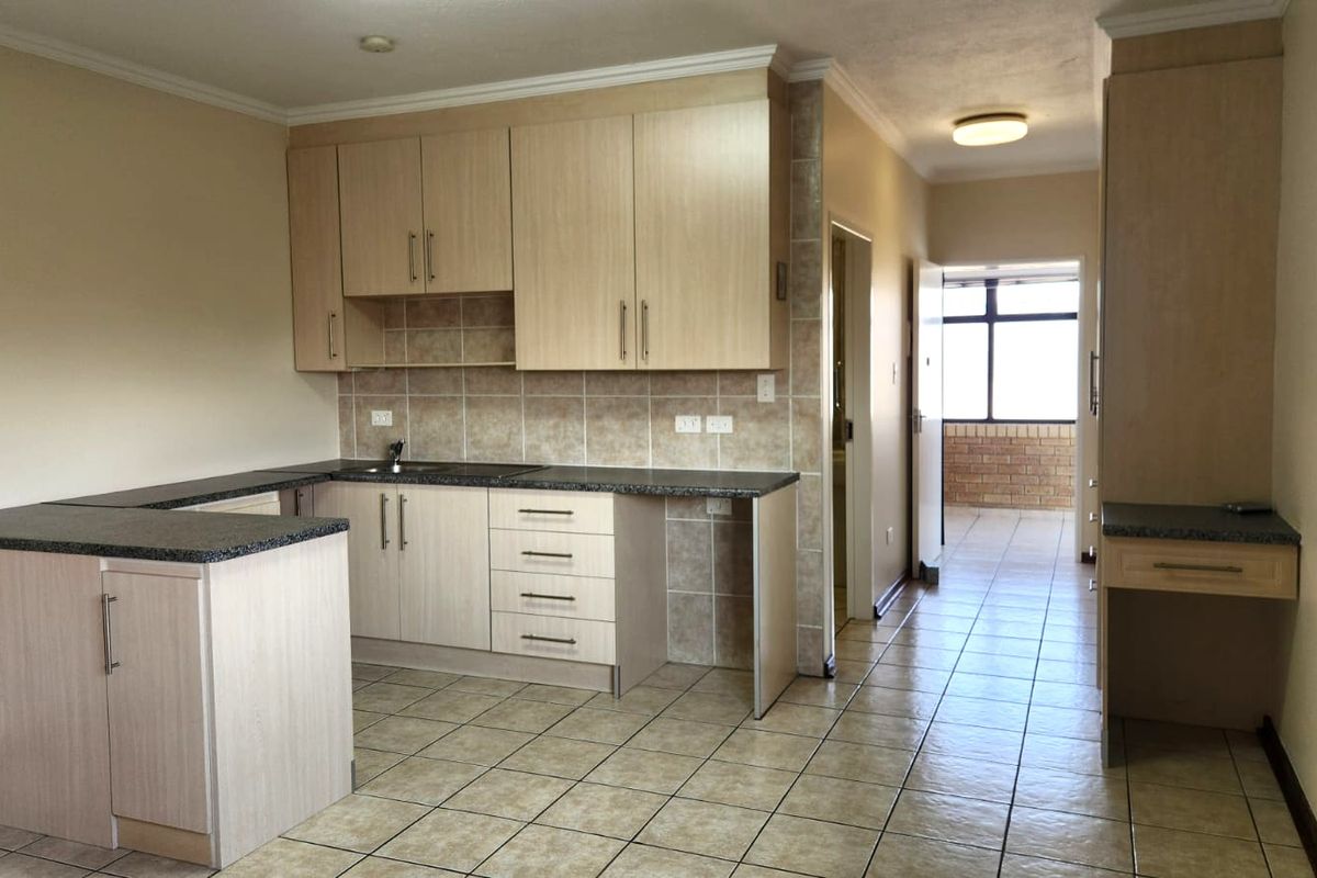 A functional kitchen featuring light wood laminate cabinetry, granite countertops, tiled backsplash, and ceramic floor tiles, with an adjacent built-in desk area.