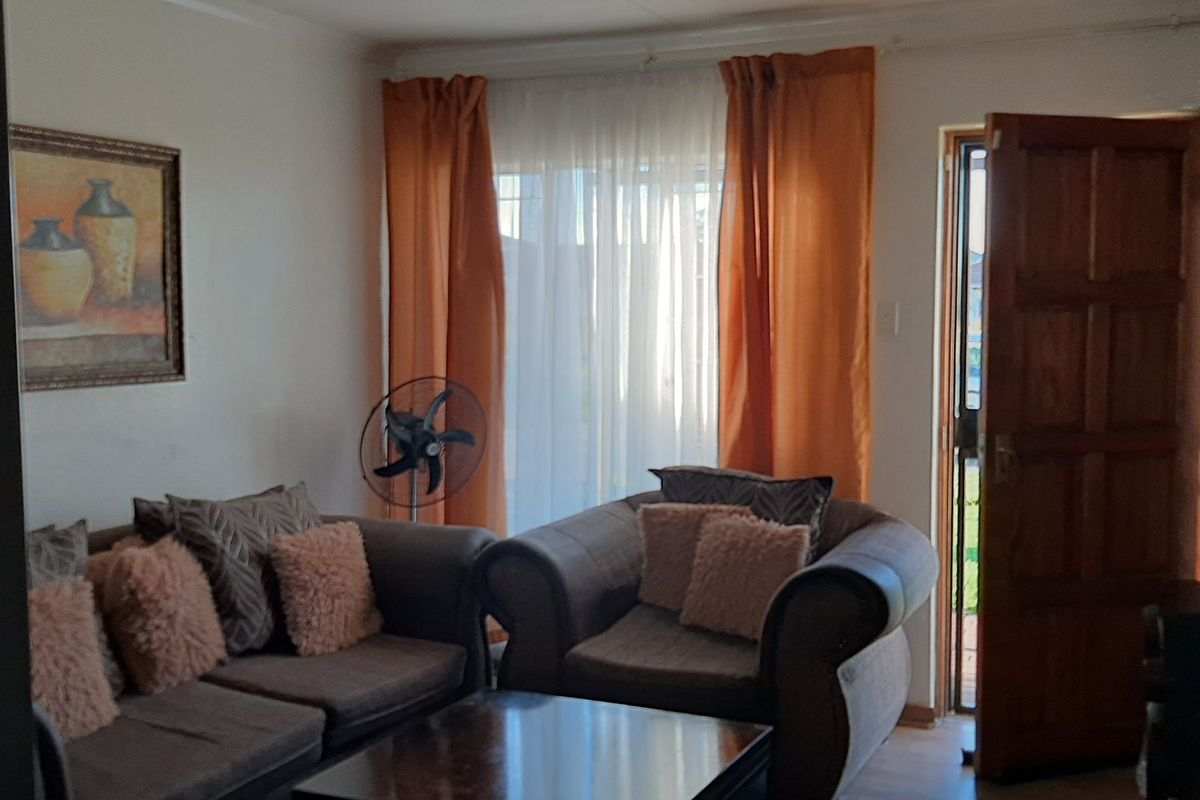 A cozy living room featuring laminate flooring, a timber entrance door, and a sliding glass door providing natural light.