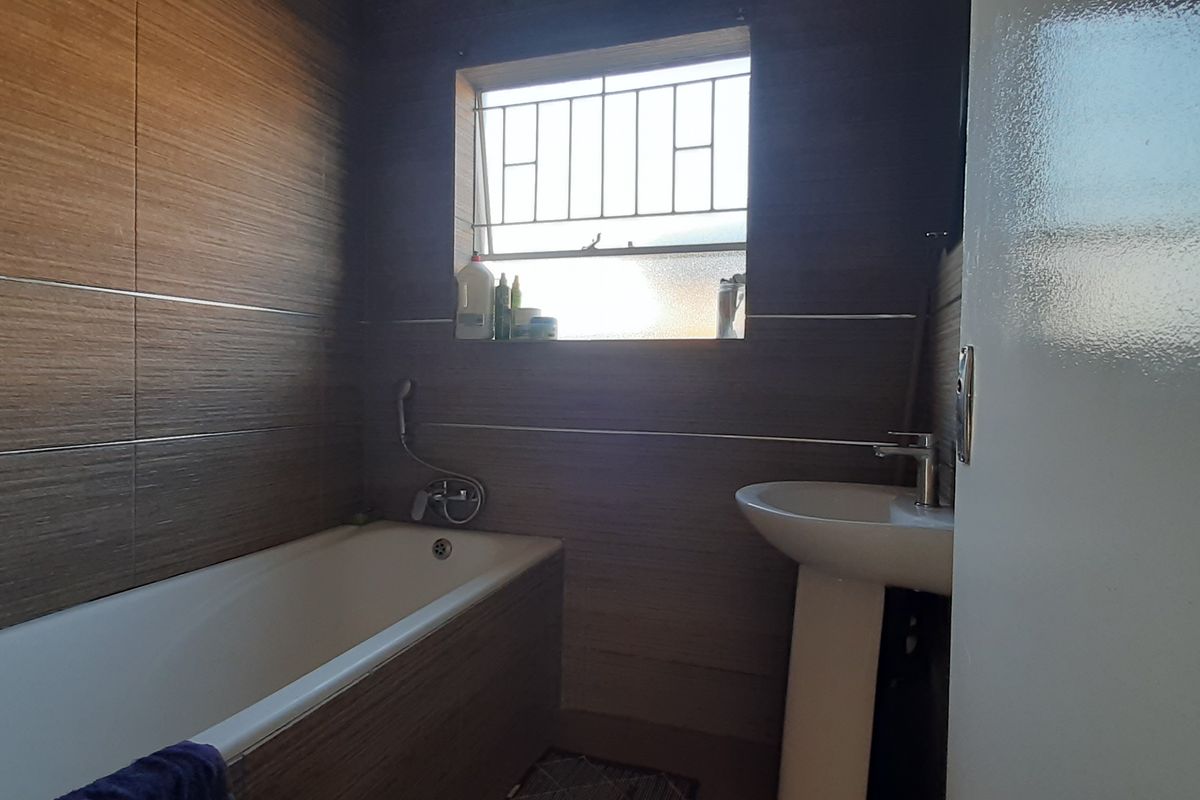 A compact bathroom featuring wood-look wall tiles, a standard bathtub, and a pedestal basin with a window providing natural light.