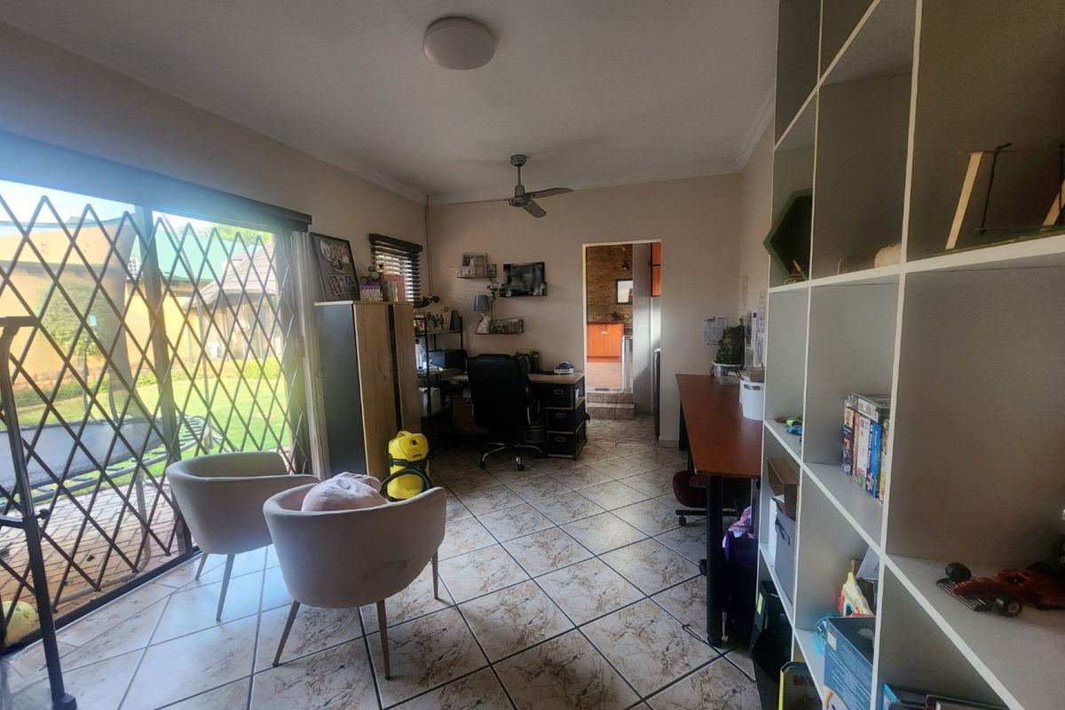 A multi-purpose living space featuring tiled flooring, a ceiling fan, and large sliding glass doors with security gates leading to the garden.