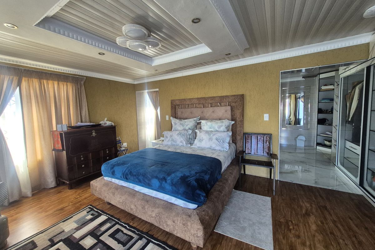 Spacious bedroom featuring a recessed ceiling with downlights, laminate flooring, and an integrated walk-in wardrobe leading to an en-suite bathroom.
