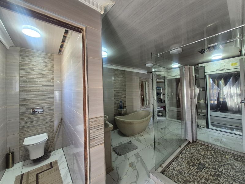 Modern bathroom featuring a freestanding bathtub, glass-enclosed shower with pebble flooring, and a separate toilet area with contemporary wall tiling.