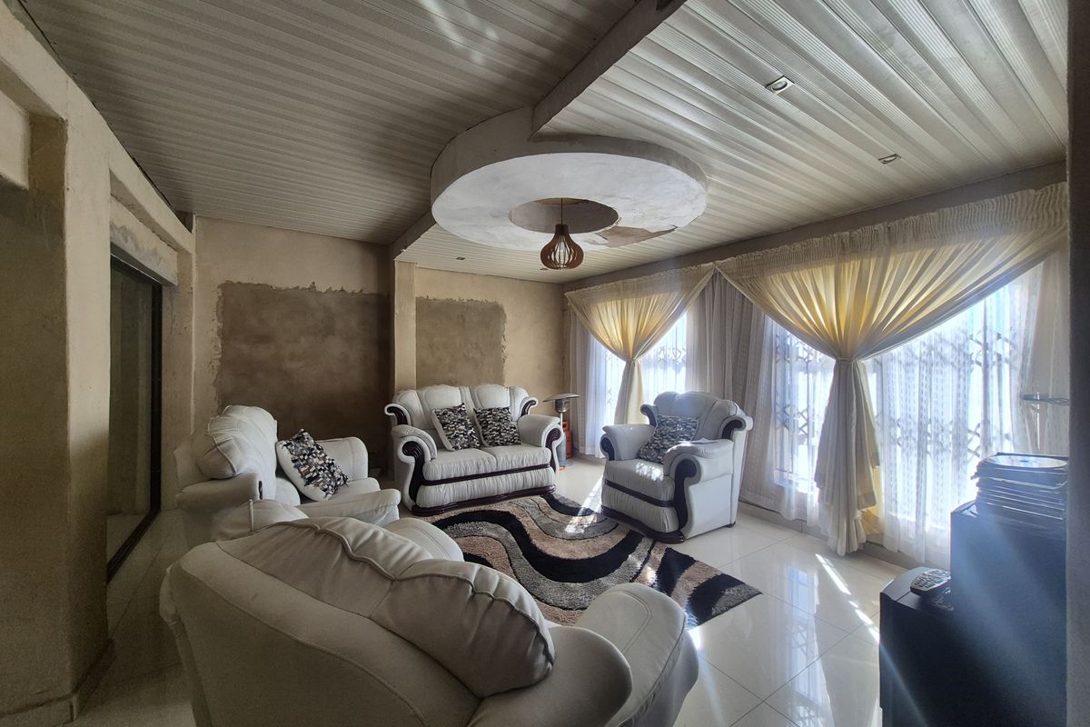 A living room featuring tiled floors and a unique ceiling design, currently requiring wall finishing and ceiling repairs to complete the space.