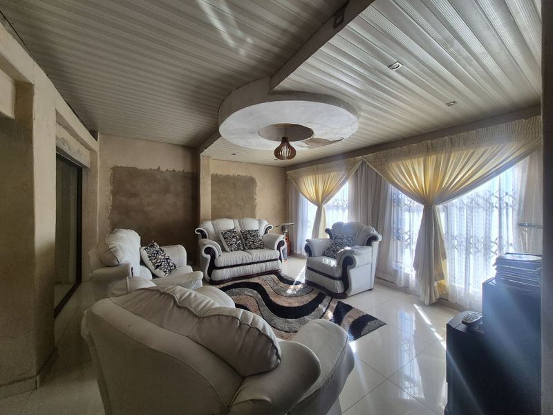 A living room featuring tiled floors and a unique ceiling design, currently requiring wall finishing and ceiling repairs to complete the space.