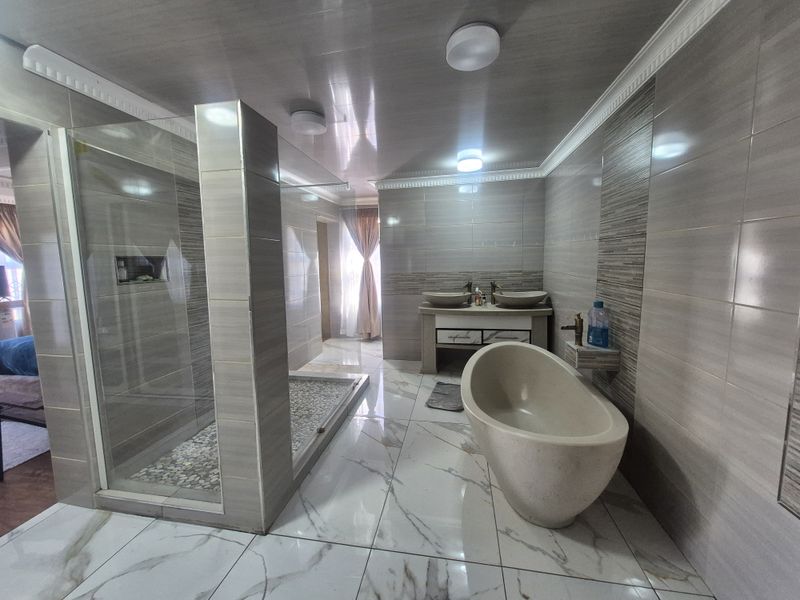 Modern bathroom featuring a freestanding bathtub, spacious walk-in shower with pebble flooring, and a double vanity with vessel sinks.