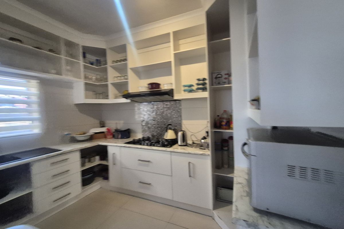 A functional kitchen featuring white built-in cabinetry, a gas hob with an extractor fan, mosaic splashback, and tiled flooring.