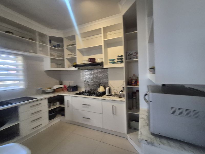A functional kitchen featuring white built-in cabinetry, a gas hob with an extractor fan, mosaic splashback, and tiled flooring.