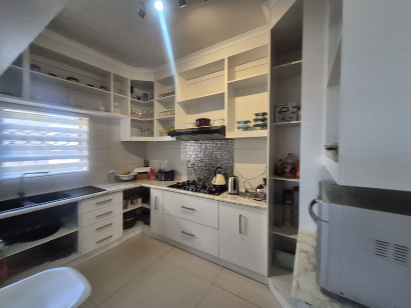 Modern kitchen featuring white cabinetry, stone countertops, gas hob with extractor fan, and a mosaic tile splashback.
