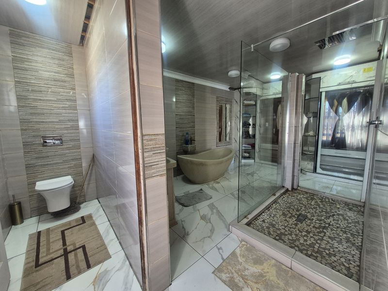 Modern bathroom featuring a freestanding bathtub, a spacious glass-enclosed shower with pebble flooring, and contemporary wall-mounted toilet with tiled finishes.