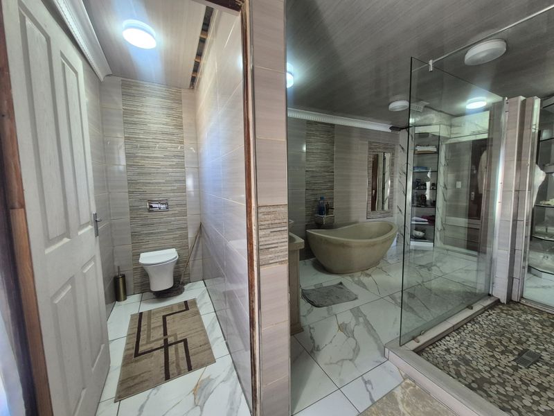 Modern bathroom featuring a freestanding bathtub, glass-enclosed shower with pebble flooring, and a separate toilet area with contemporary wall tiling.