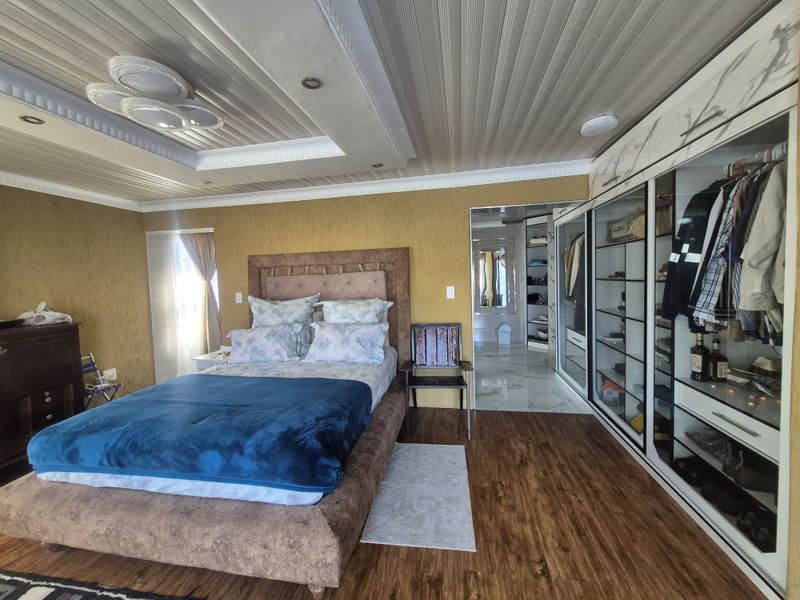Spacious bedroom featuring built-in wardrobes, textured walls, recessed ceiling lighting, and laminate flooring, with an adjoining en-suite bathroom visible.