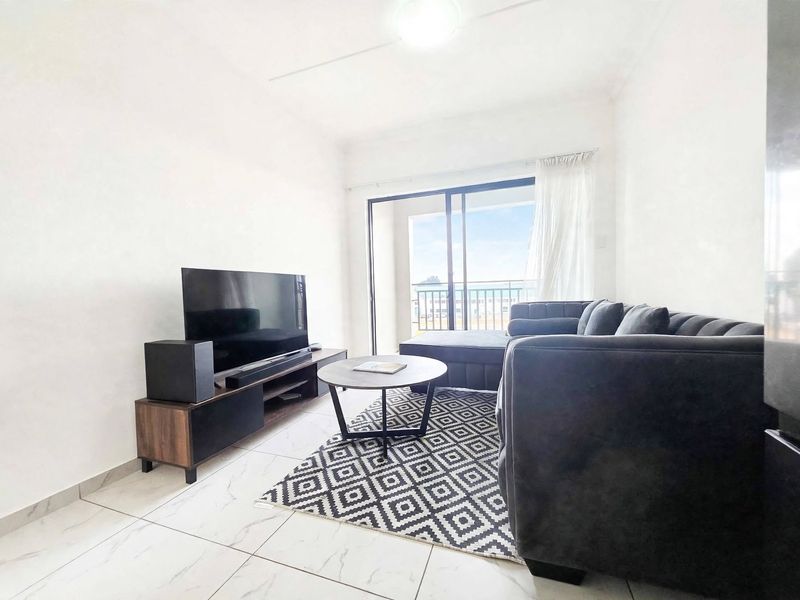 A bright living room featuring modern tiled flooring and a large sliding glass door that provides access to an outdoor balcony area.