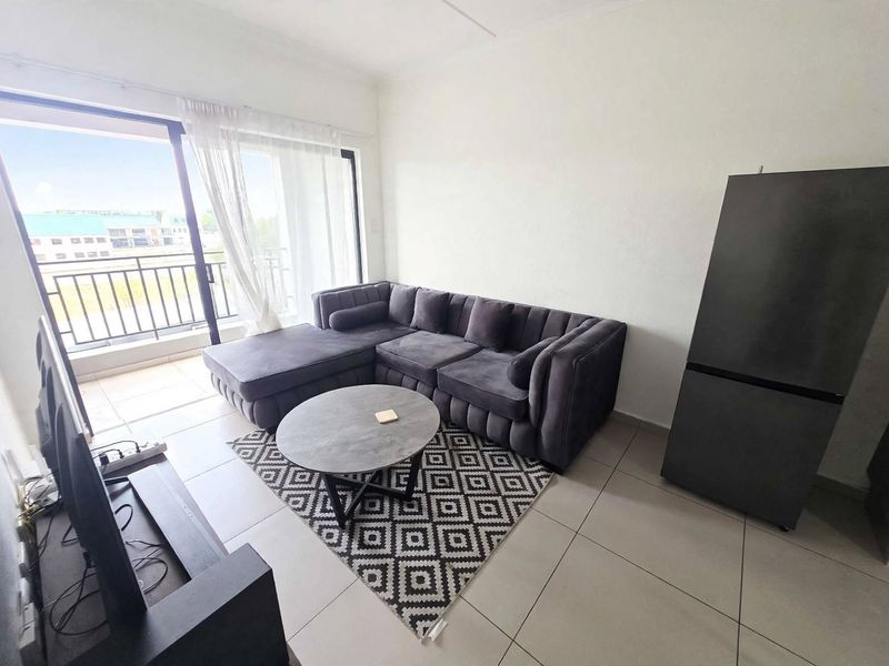 A bright living room featuring large sliding glass doors that open onto a balcony, with neutral tiled flooring throughout.