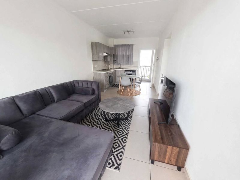 Open-plan living area featuring a modern kitchen with built-in cabinetry, hob, and oven, flowing into a comfortable lounge space with balcony access.