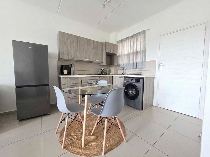 Open-plan kitchen area featuring modern wood-look cabinetry, tiled flooring, and integrated appliance connections, seamlessly flowing into the living space.