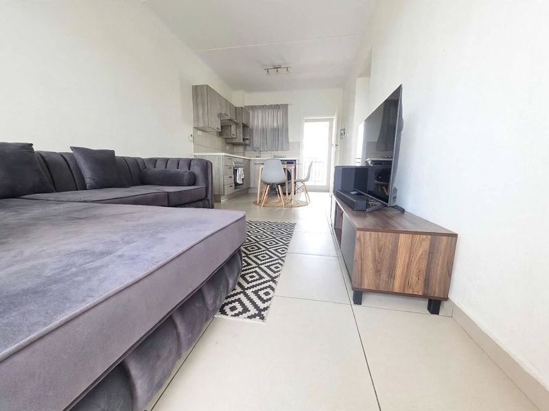 Open-plan living area featuring tiled flooring and a compact kitchen with built-in cabinetry, leading to a balcony through a glass sliding door.