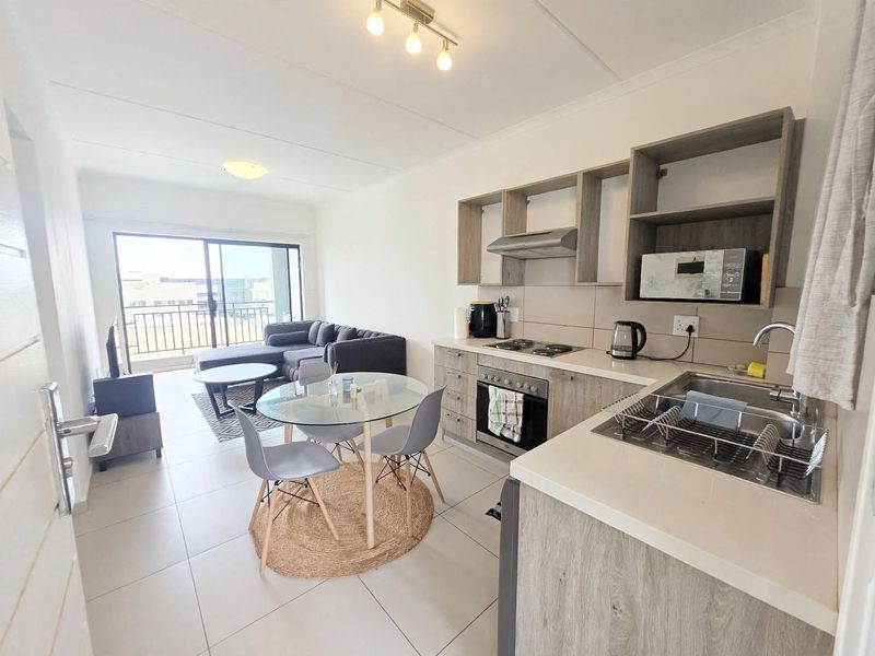 Modern open-plan apartment featuring a functional kitchen with built-in cabinetry and appliances, flowing into a living area with access to a private balcony.
