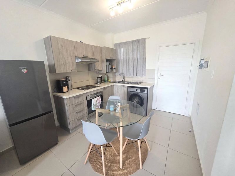 Compact kitchen featuring modern wood-look cabinetry, built-in oven and hob, stainless steel sink, and integrated laundry appliance with tiled flooring.