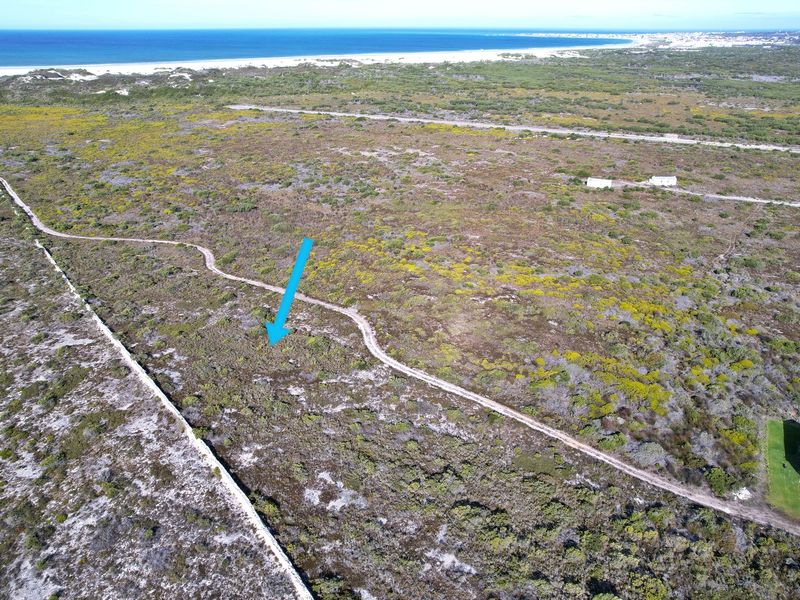 Aerial view of a vacant residential plot featuring natural coastal vegetation, a dirt access track, and proximity to the beach.