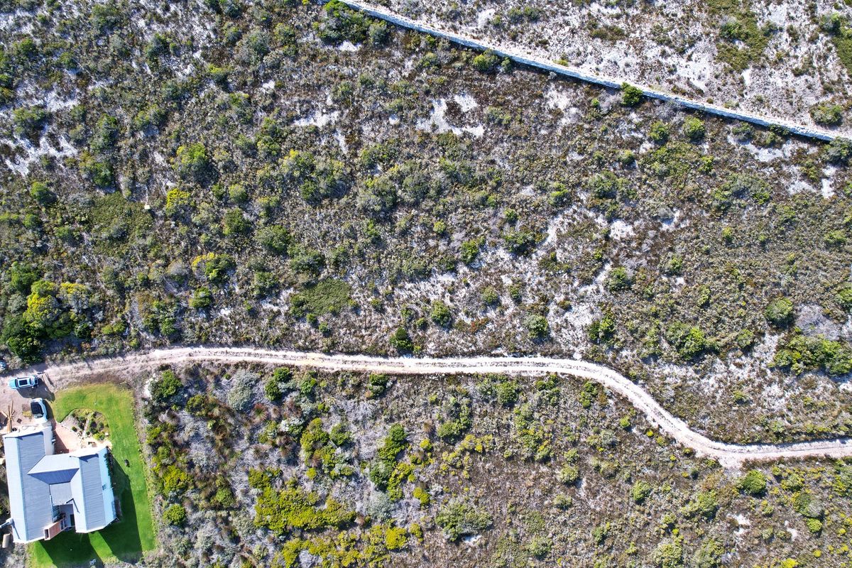 Aerial view of a vacant residential plot featuring natural vegetation, a stone boundary wall, and a dirt access track.