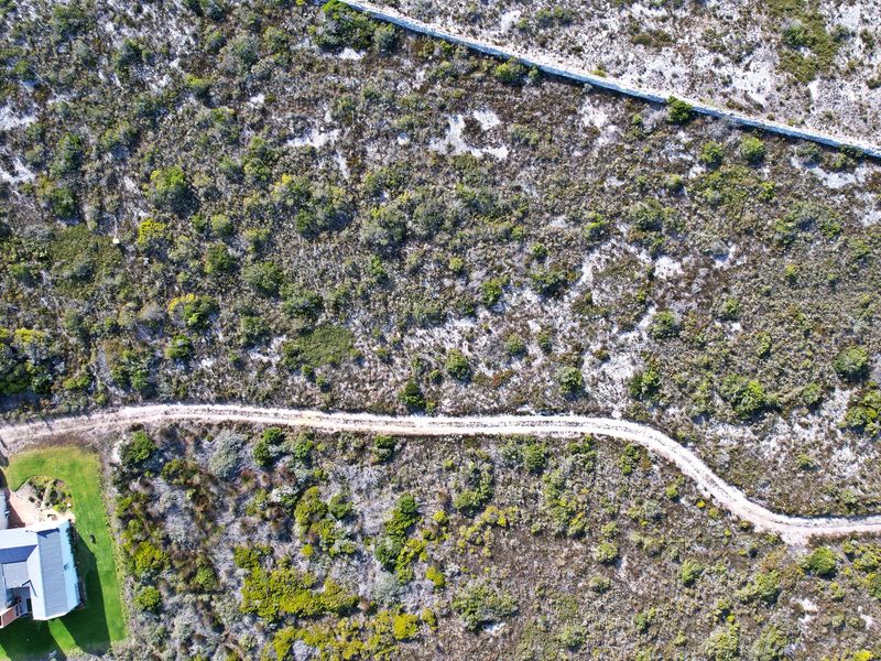 Aerial view of a vacant residential plot featuring natural vegetation, a stone boundary wall, and a dirt access track.