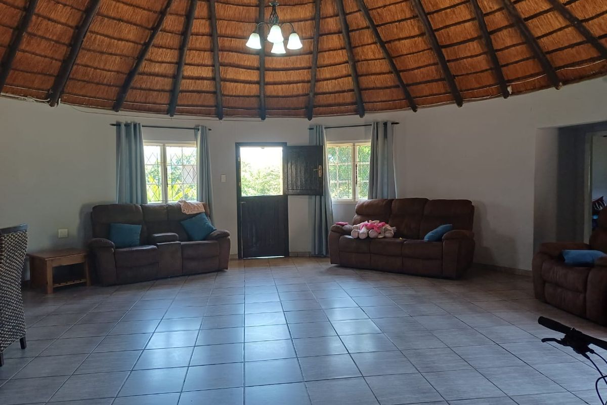 Spacious living area featuring a unique circular layout with a traditional thatched roof, exposed timber rafters, and neutral ceramic floor tiles.