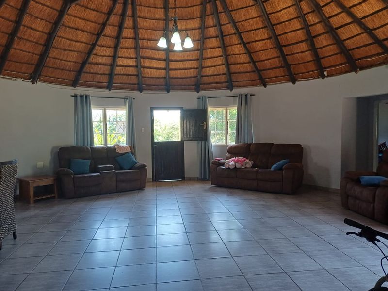 Spacious living area featuring a unique circular layout with a traditional thatched roof, exposed timber rafters, and neutral ceramic floor tiles.