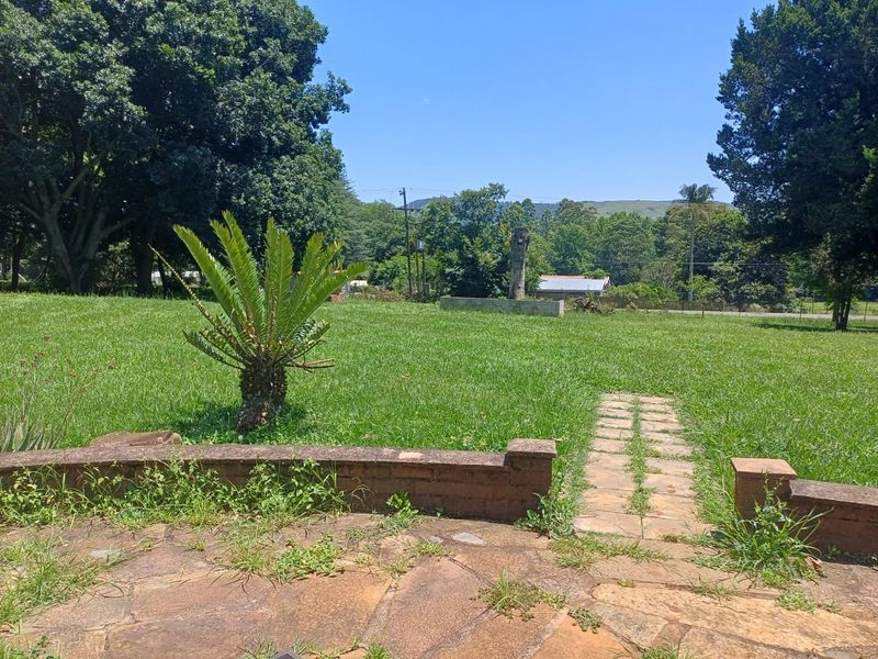 A spacious garden area featuring a stone-paved patio, a brick retaining wall, and a stone pathway leading through a large lawn.