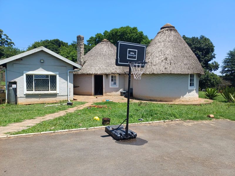 Rear view of the property featuring a traditional thatched roof structure, stone chimney, and a paved patio area set within a garden.